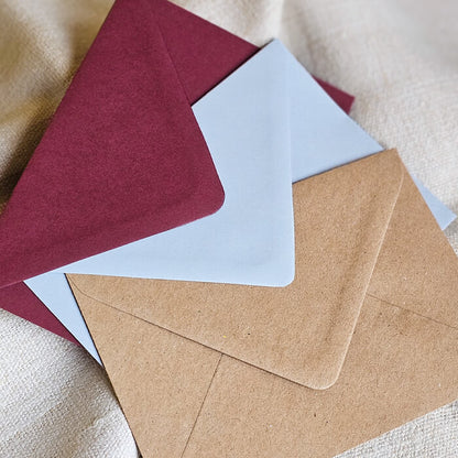 Raznobojne kuverte za pozivnice za vjenčanje uključujući bordo, plavu i smeđu na tekstilnoj podlozi